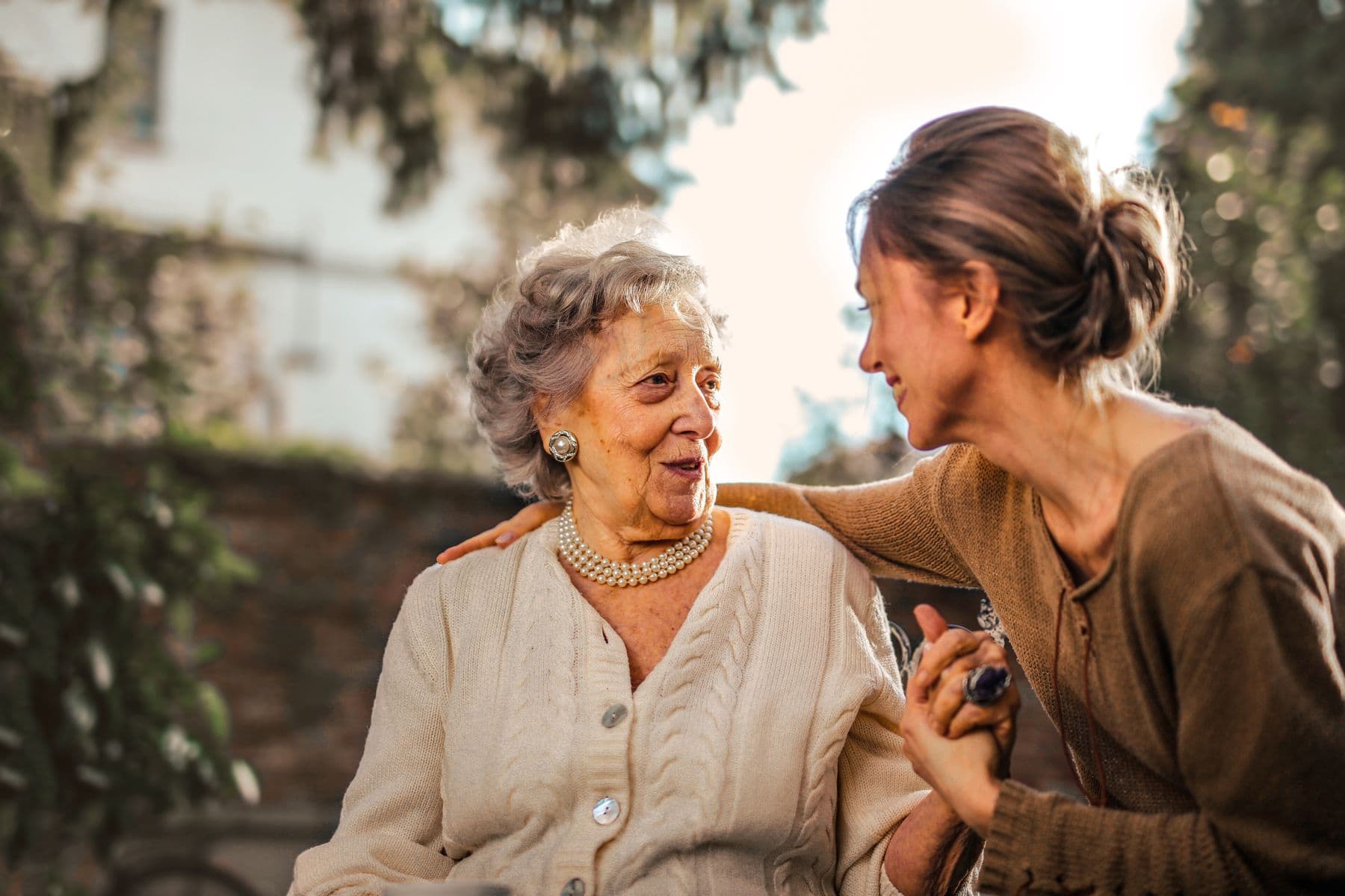 A caregiver sitting beside an older woman and sharing a warm conversation outdoors